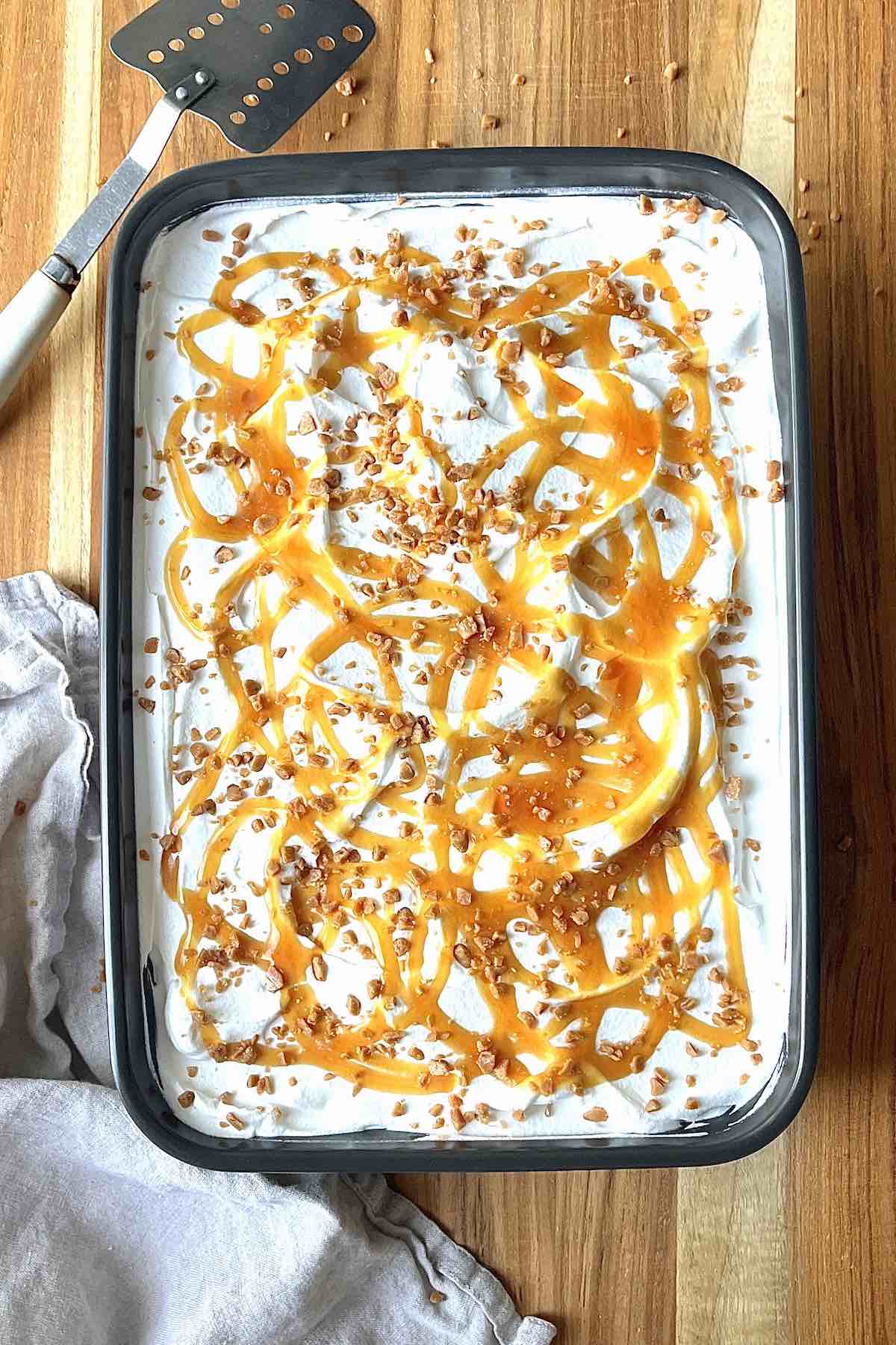 Pumpkin poke cake on a wooden table with a beige linen and serving spatula next to it.