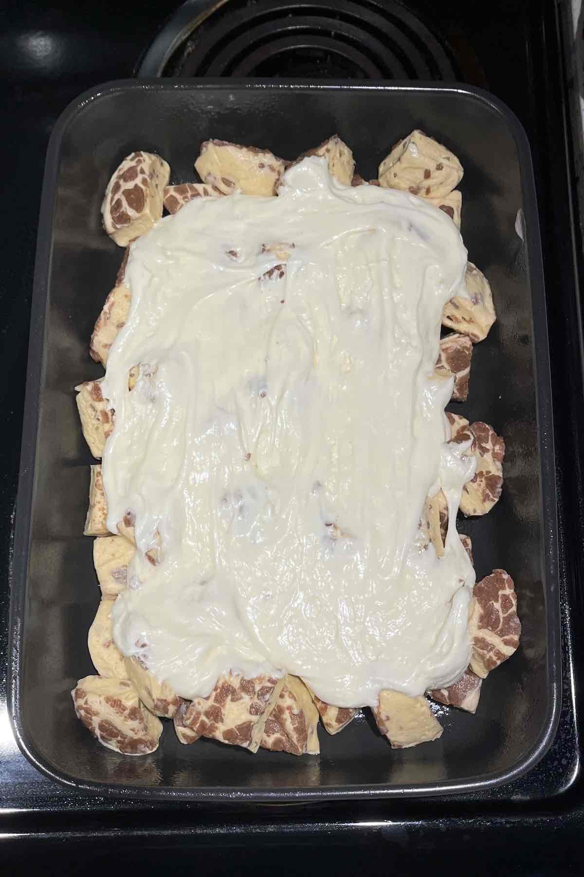 Cinnamon roll pieces and frosting in a baking dish.
