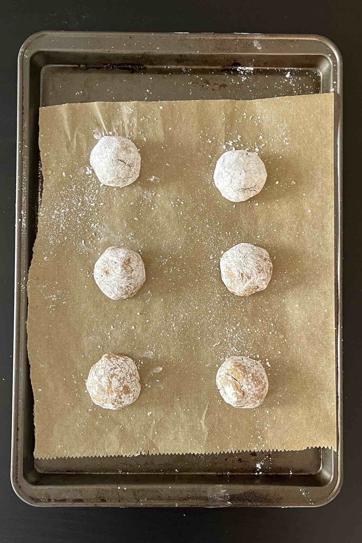 Coated pumpkin crinkle cookie dough balls lined on a baking sheet.