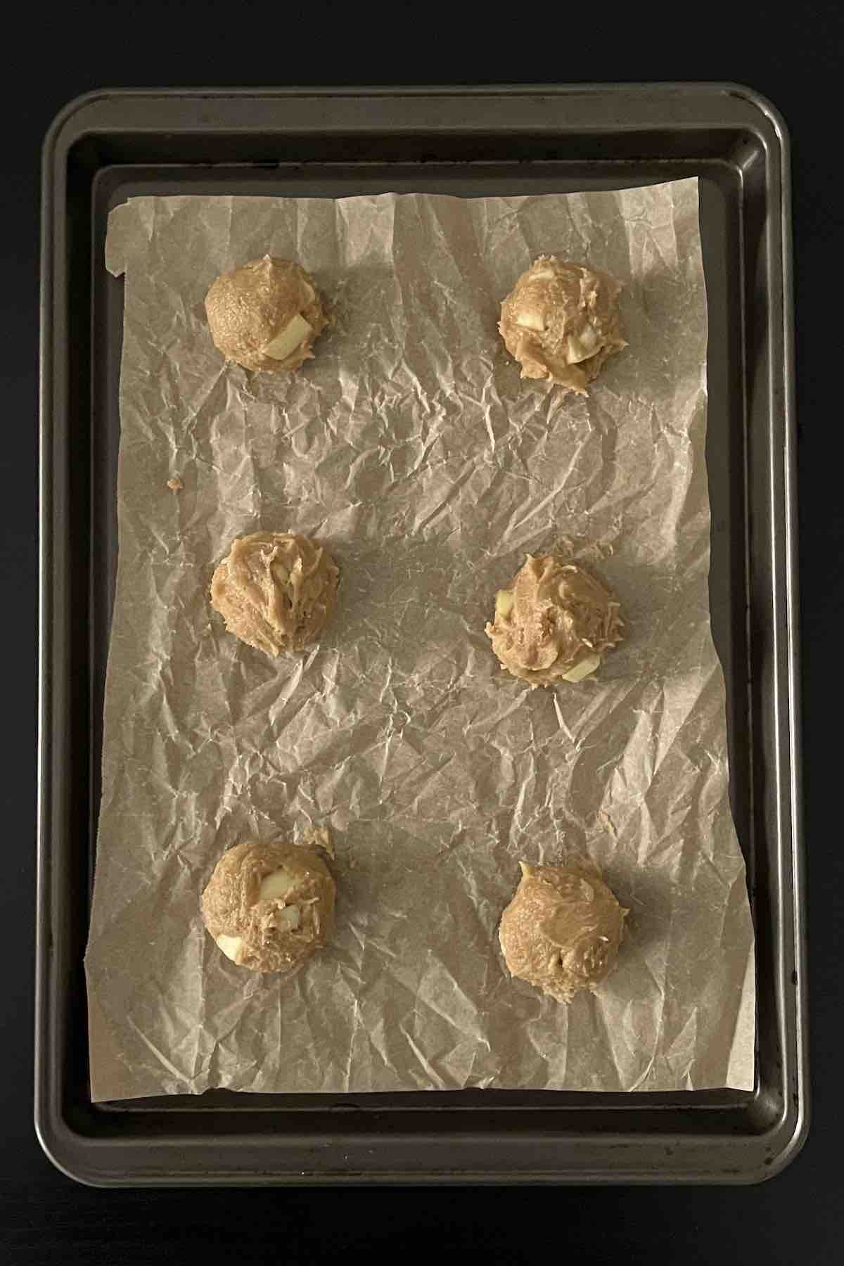 Cookie dough balls on a lined baking sheet.