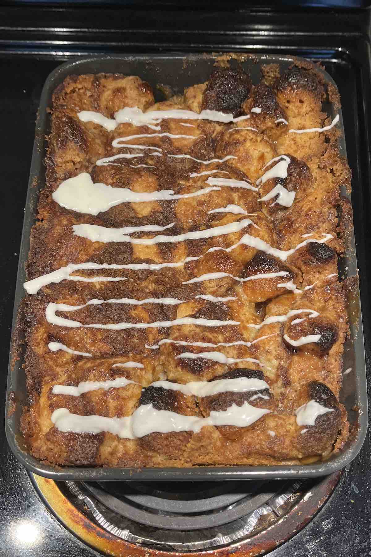 Baked cinnamon roll dump cake with icing on top of it in a baking dish.
