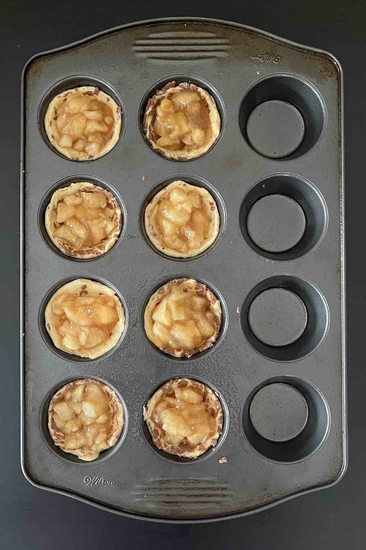 Cinnamon roll dough filled with apple pie filling in a muffin pan.