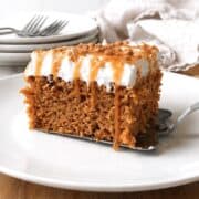 Slice of pumpkin poke cake on a white plate with a serving spatula under it.