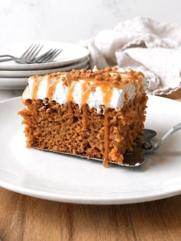 Slice of pumpkin poke cake on a white plate with a serving spatula under it.