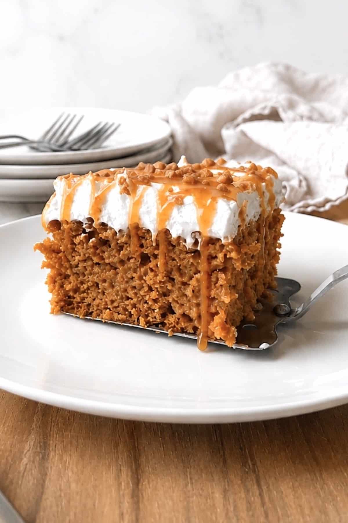 Slice of pumpkin poke cake on a white plate with a serving spatula under it.