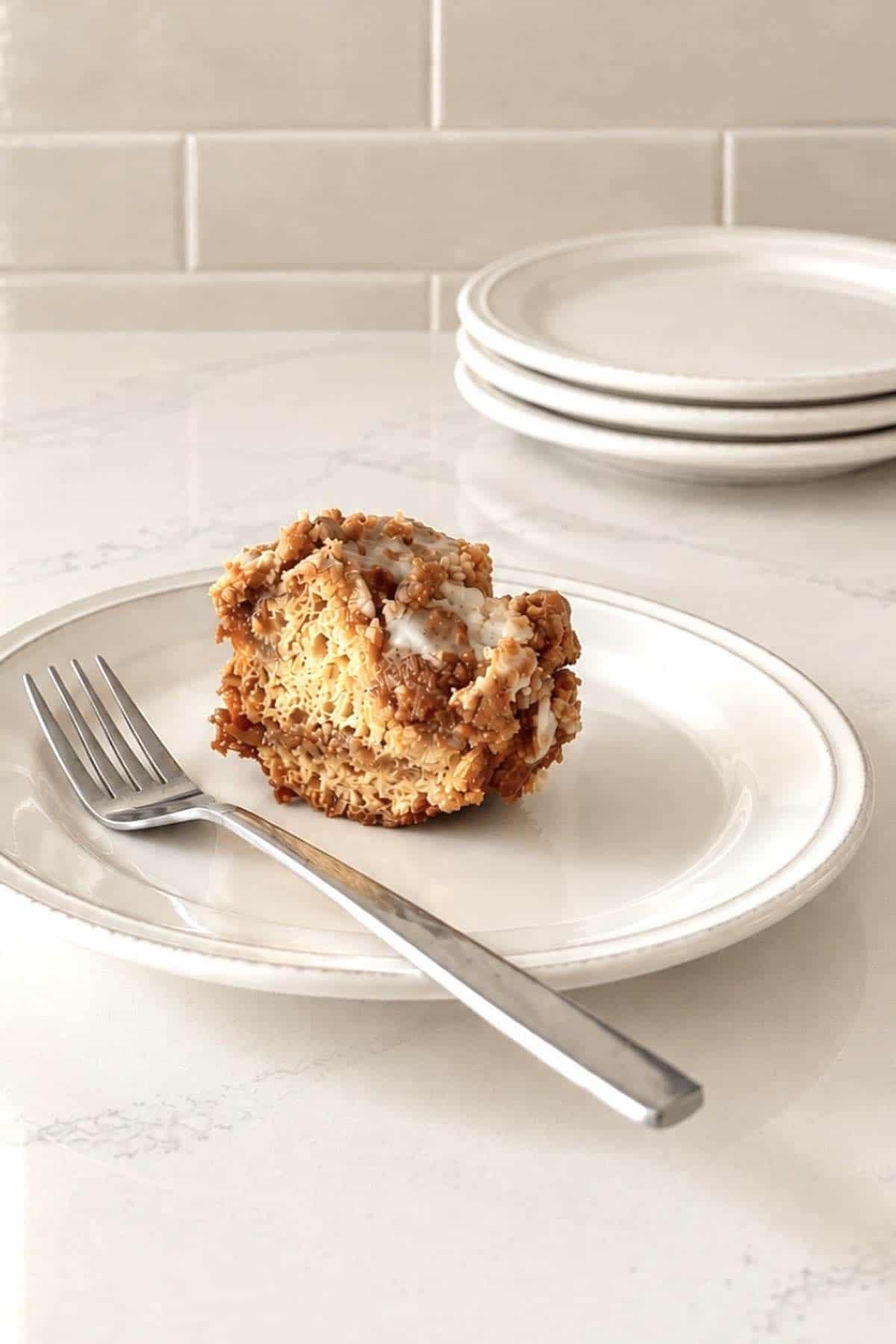 Slice of iced apple pie filling cake on a white plate with a fork on it.