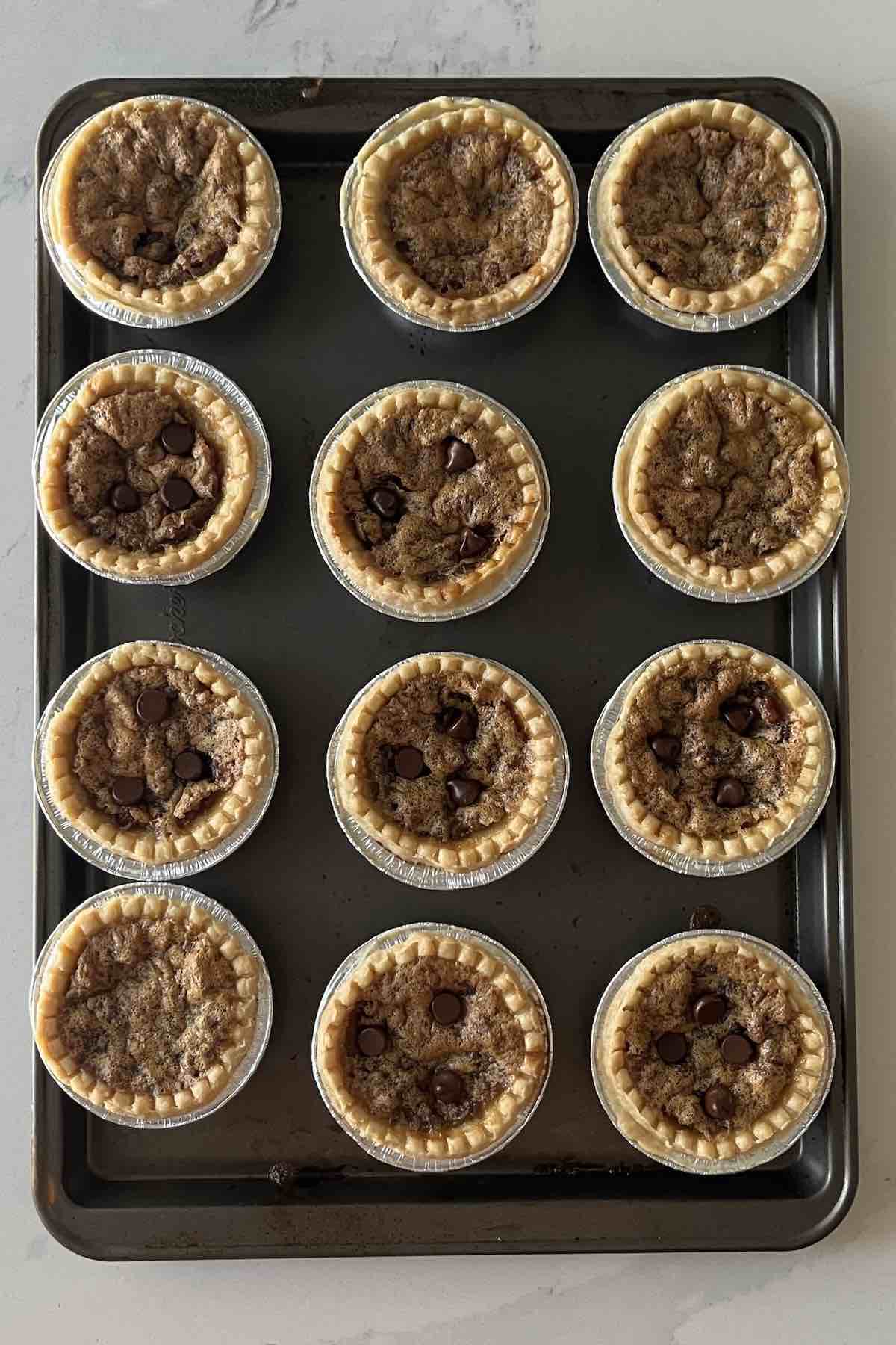Baked chocolate pecan butter tarts lined on a baking sheet.