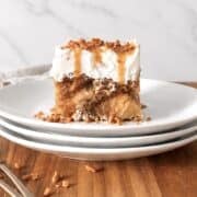 Slice of caramel apple poke cake on a stack of 3 white plates.