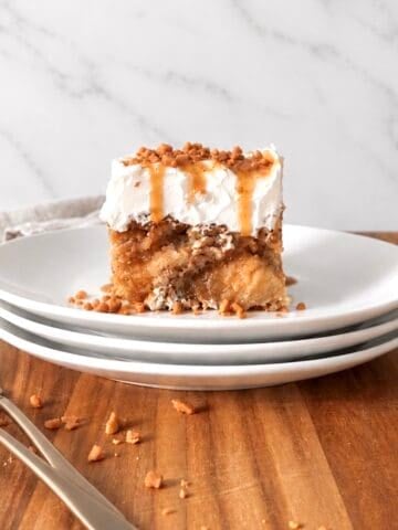 Slice of caramel apple poke cake on a stack of 3 white plates.