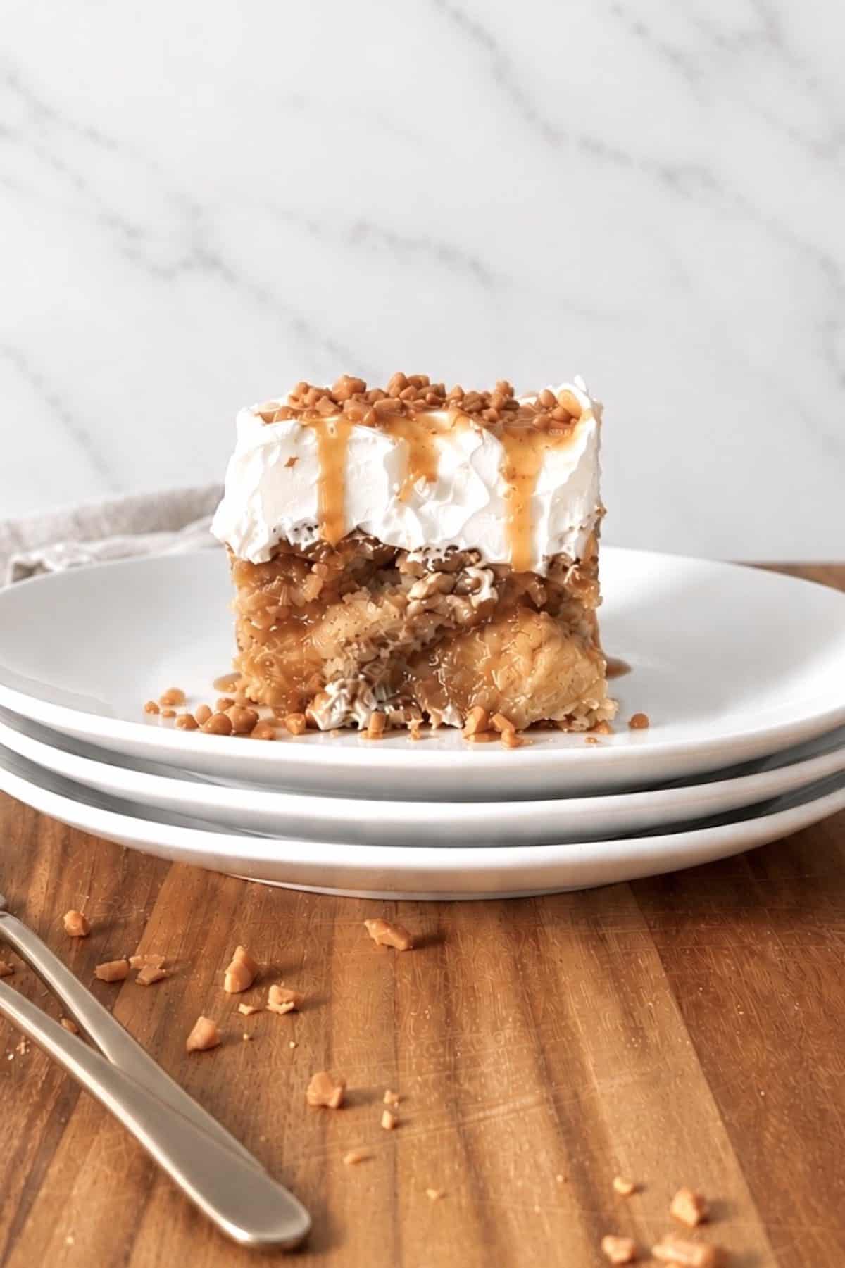 Slice of caramel apple poke cake on a stack of 3 white plates.