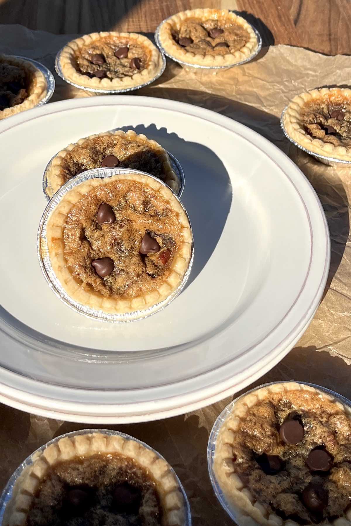 Two chocolate pecan butter tarts on a stack of white plates.