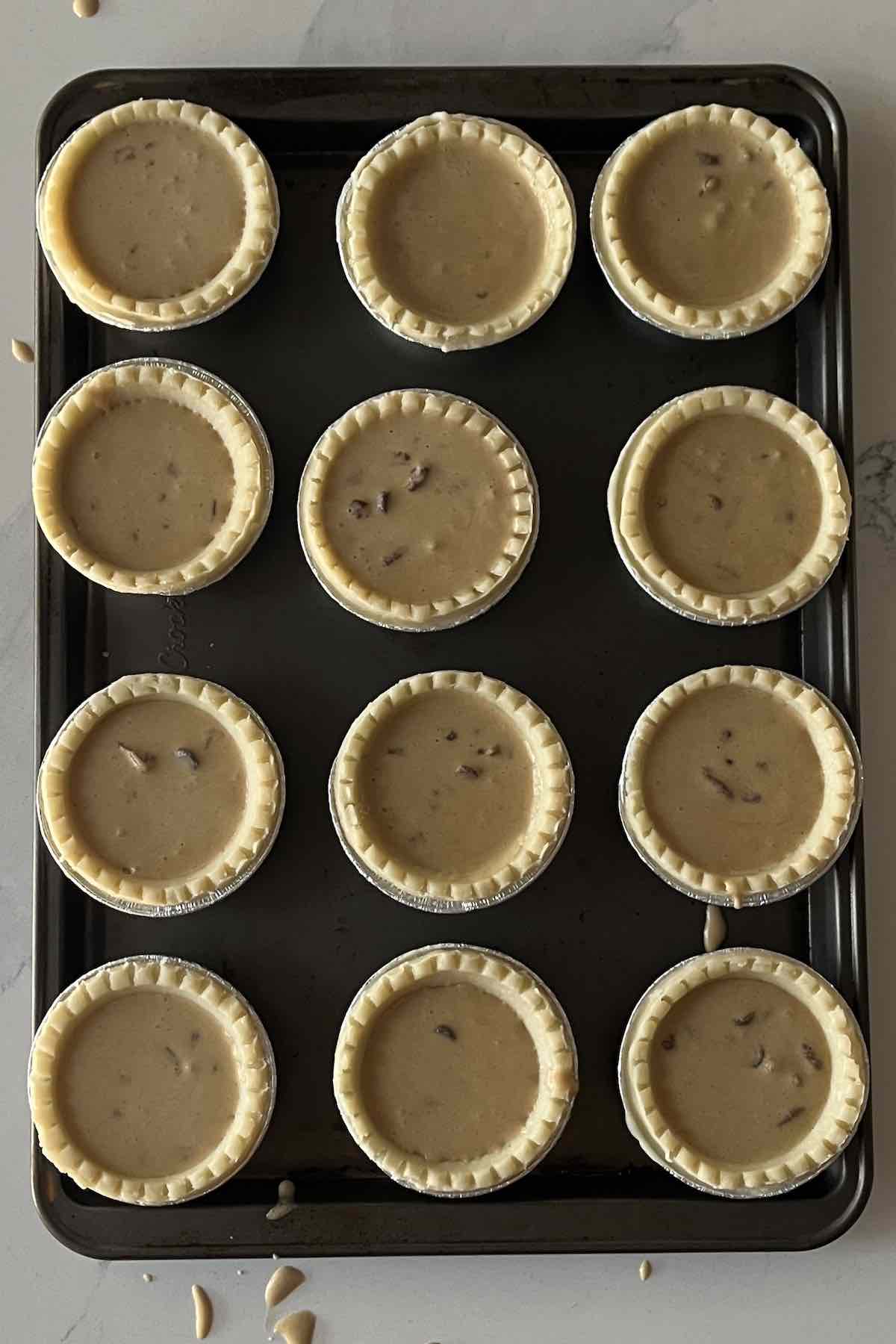 Tart shells on a baking sheet filled with the chocolate pecan butter tart filling.